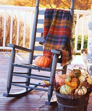 rocking chair  outdoors on porch with fall tartan blanket and a barrel of pumpkins and other decorations