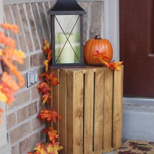 wood crate topped with pumpkin, lantern and fall garland on front porch