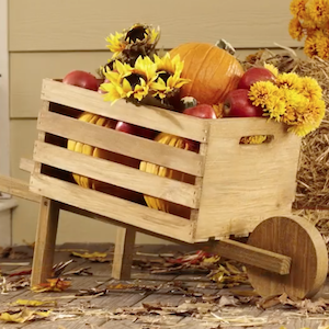 carretilla al aire libre con decoraciones de otoño en el interior como calabazas, manzanas y flores de otoño