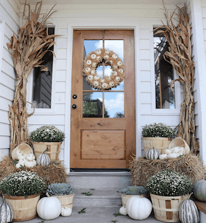 neutral fall porch decor with dried corn, hay bales, white pumpkins and mums