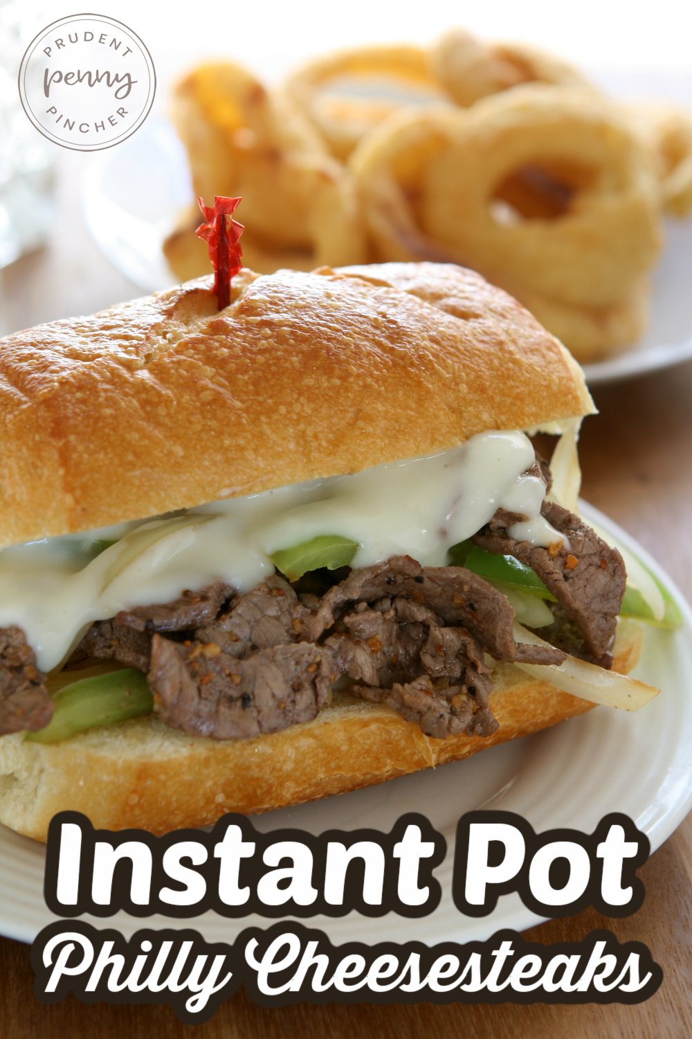 Philly cheesesteaks on a plate with a side of onion rings in the background