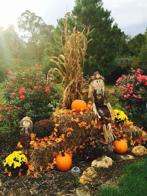 outdoor fall yard decorations with hay bales, scarecrows, maple leaf garlands and pumpkins
