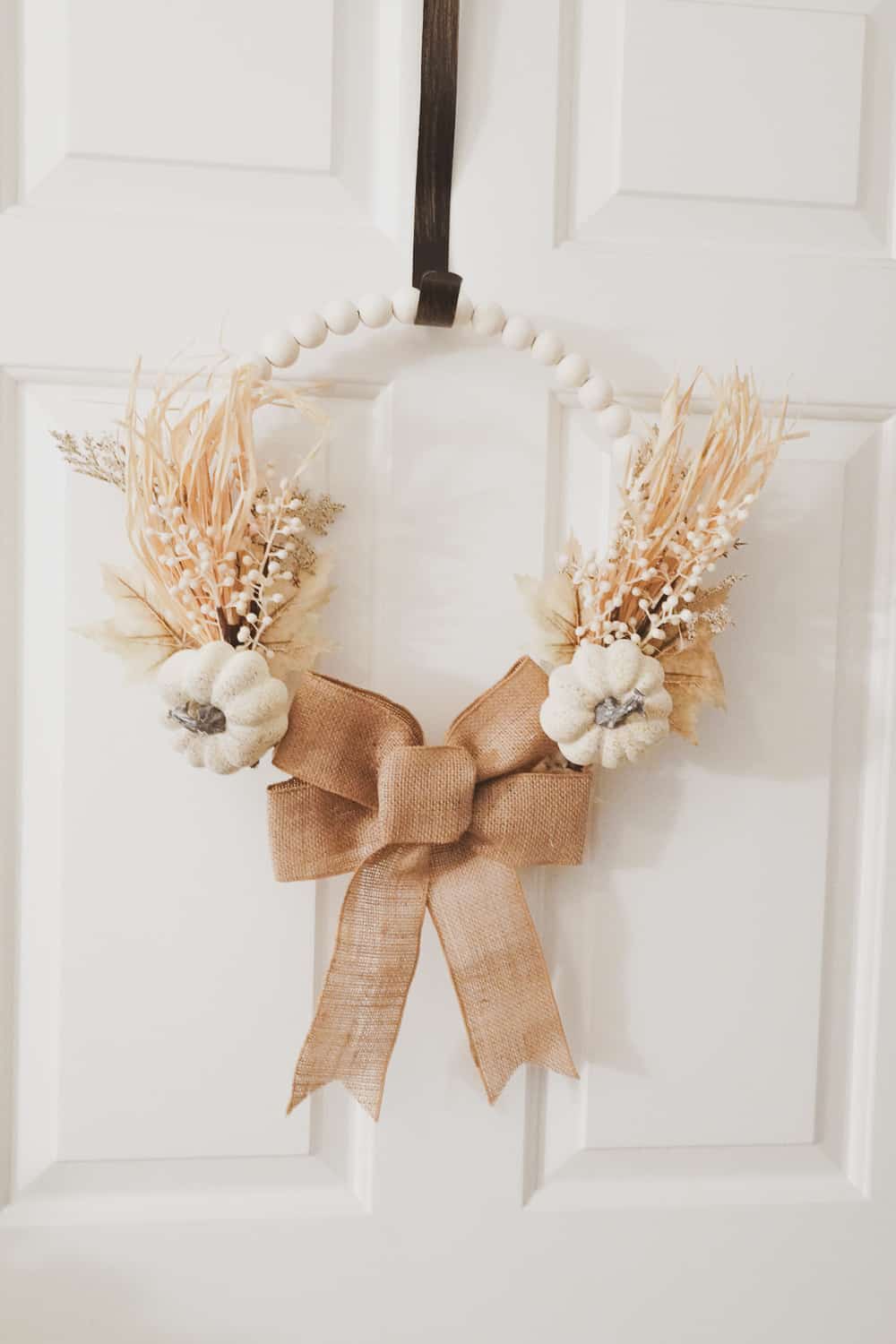 wood bead fall wreath that has a burlap bow on bottom with two neutral fall picks on the side