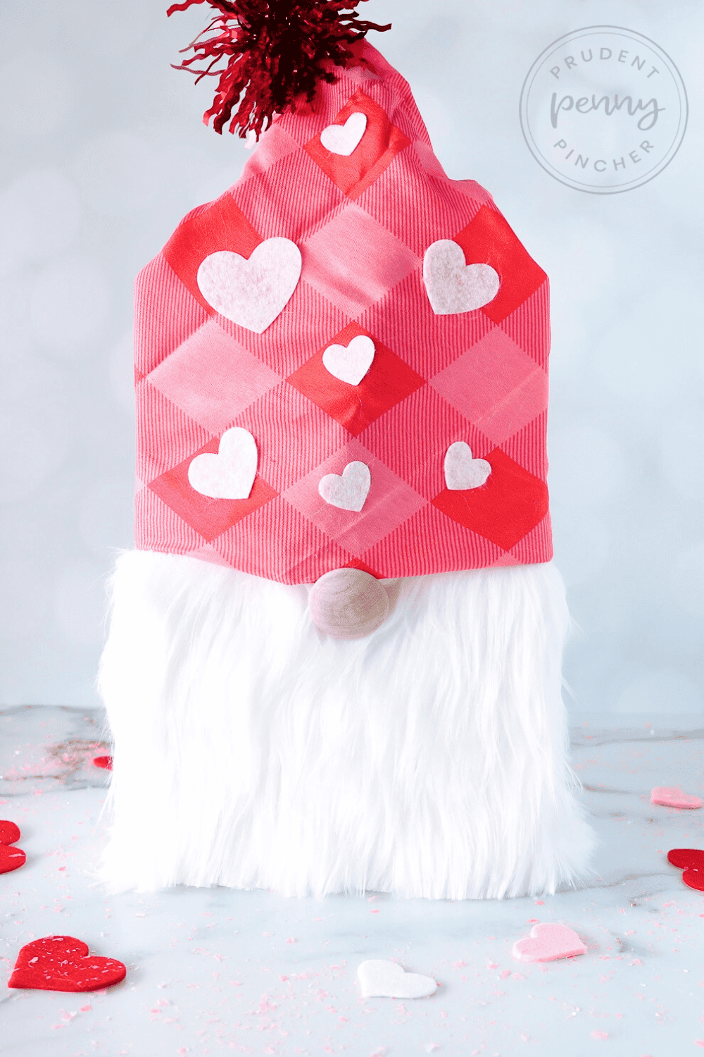 Homemade gnome Valentine box with a pink plaid bandana hat decorated with felt hearts and a shiny red tinsel pom-pom.