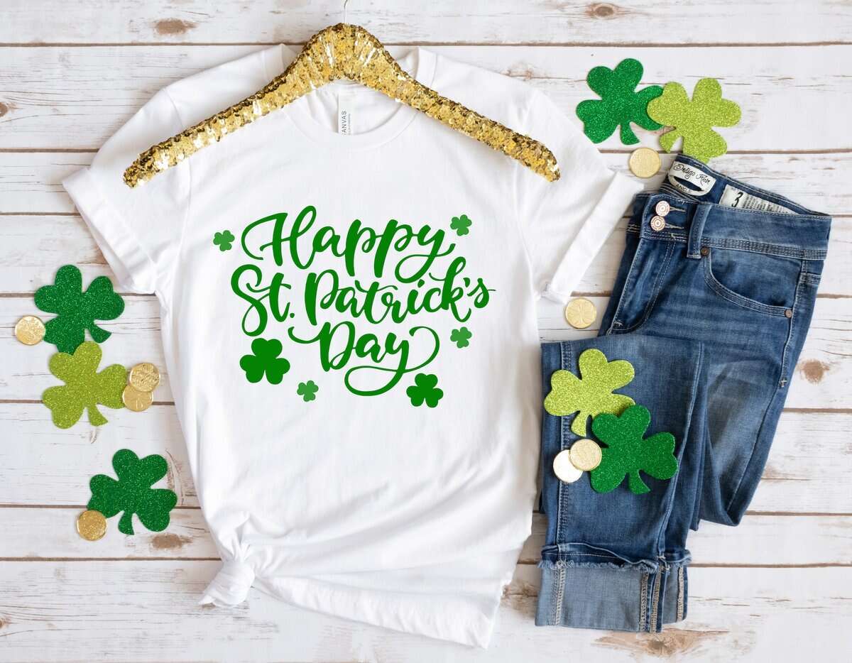 shirt mockup with green script design, shamrocks, and jeans flat lay